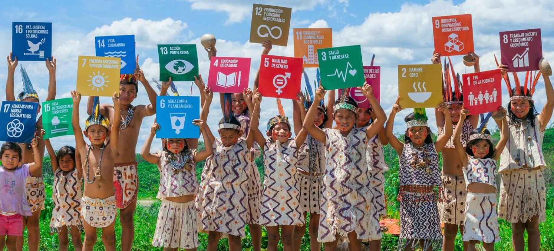 En un área verde, un grupo de niños y niñas sostienen en alto carteles de los Objetivos de Desarrollo Sostenible.