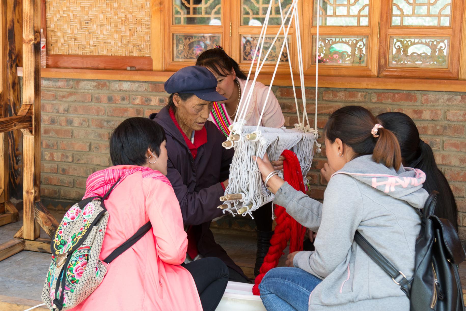 Quatre jeunes filles chinoises sont assises autour d'une femme âgée et la regardent tisser de la laine. 