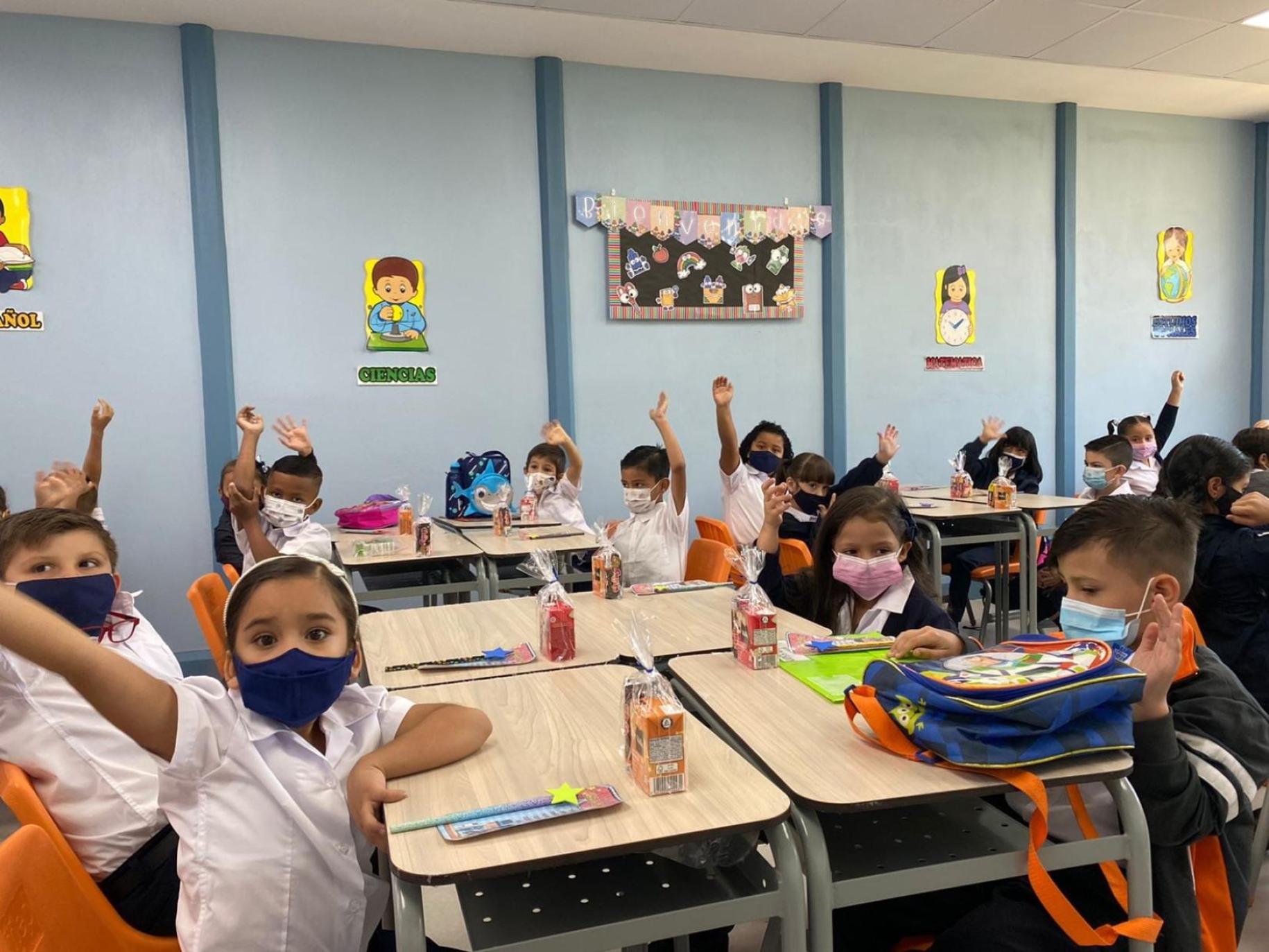 一群学龄儿童在教室里相邻而坐，在课堂上举手。