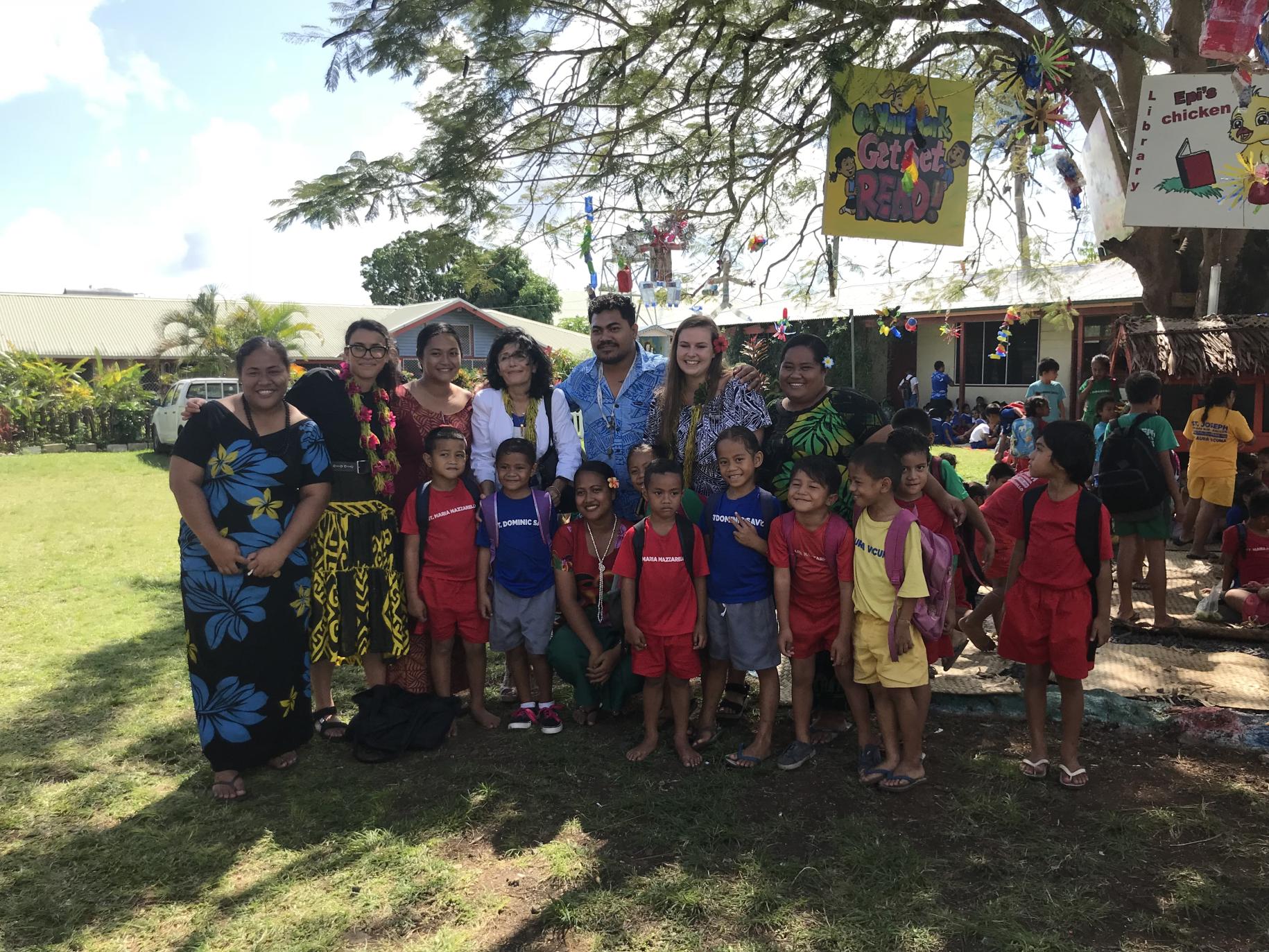 7 adults and 9 children stading under a tree in an education-related event