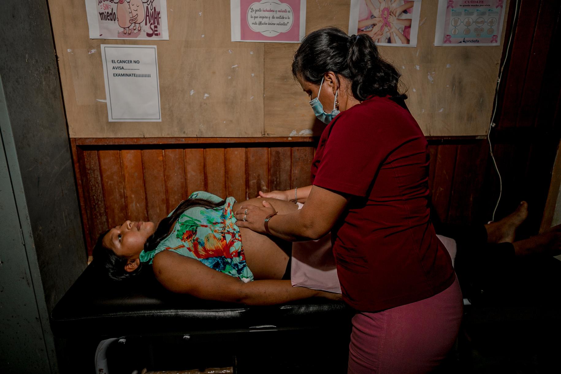 Personal sanitario auscultando a una paciente que se encuentra acostada sobre una camilla negra.