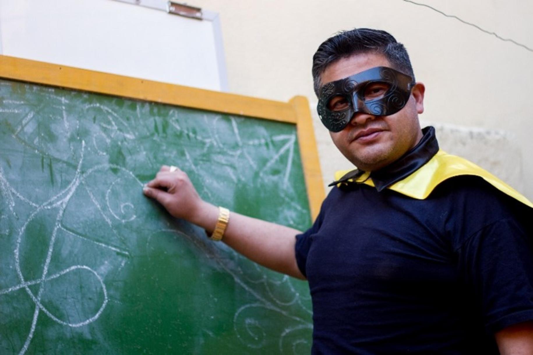 穿着服装的玻利维亚超级教师，手里拿着粉笔在黑板前。