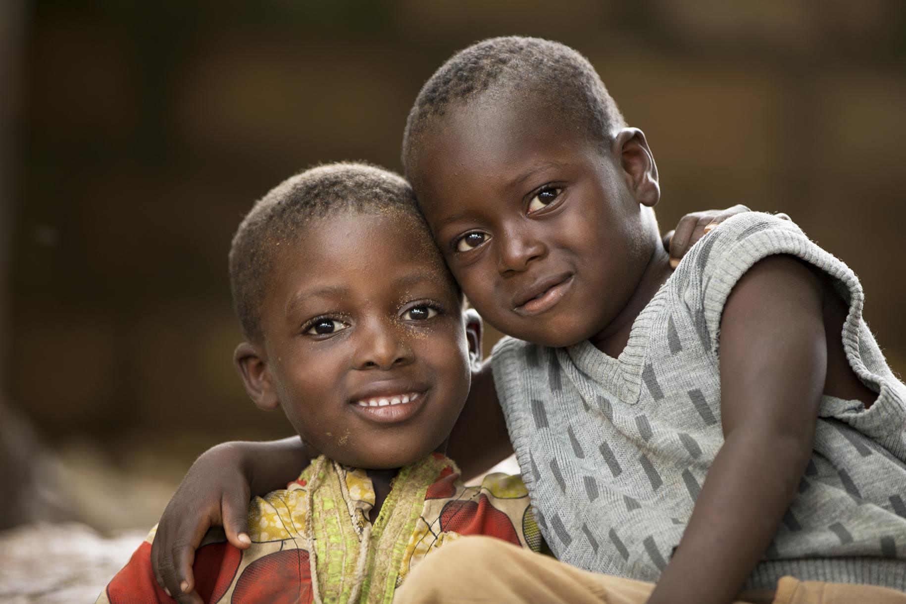 Au Togo, deux jeunes garçons sont assis côte à côte, le bras de l'un posé autour des épaules de l'autre, et regardent l'objectif de la caméra en souriant, l'air fier.