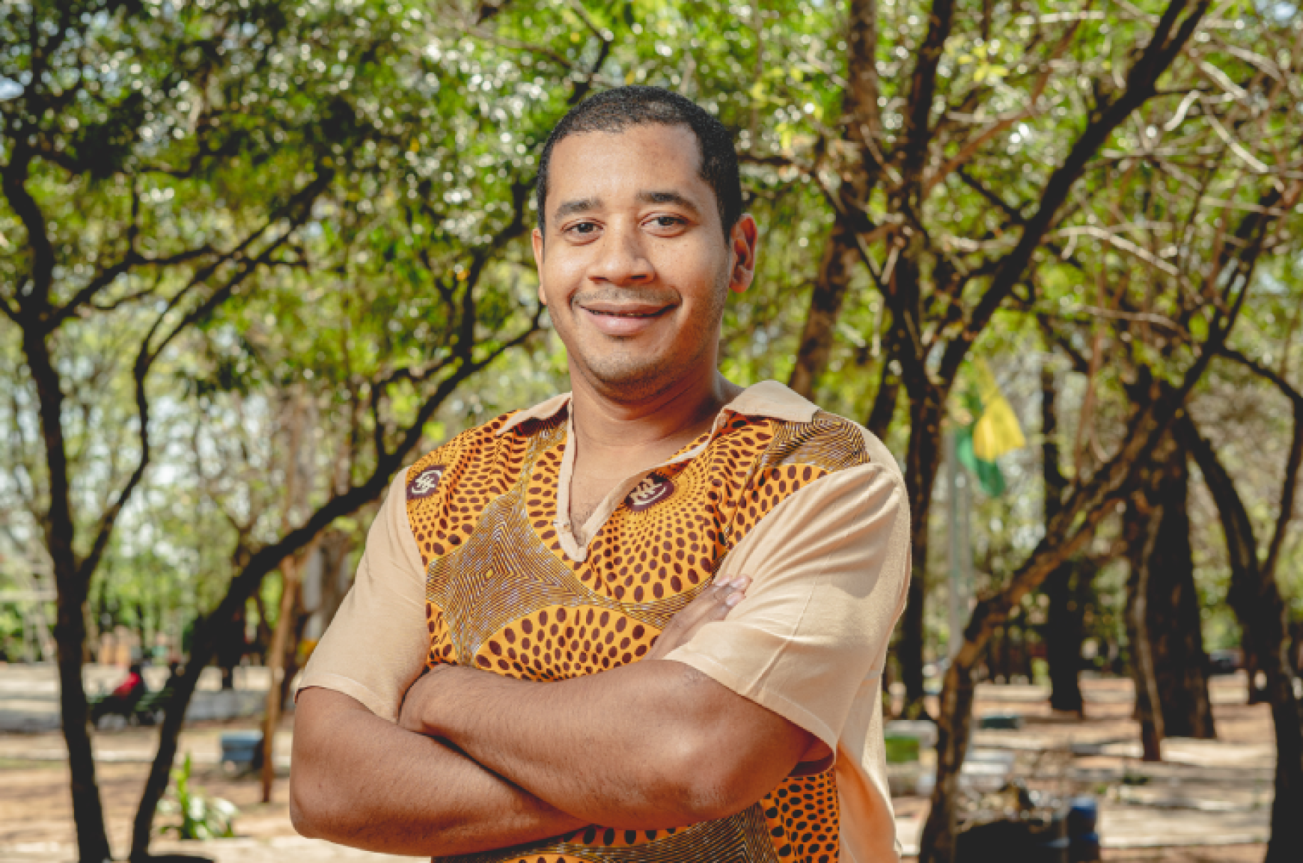 Au Paraguay, un homme portant une chemise de couleur moutarde pose devant la caméra, les bras croisés, en soutiant, au milieu d'un espace boisé.