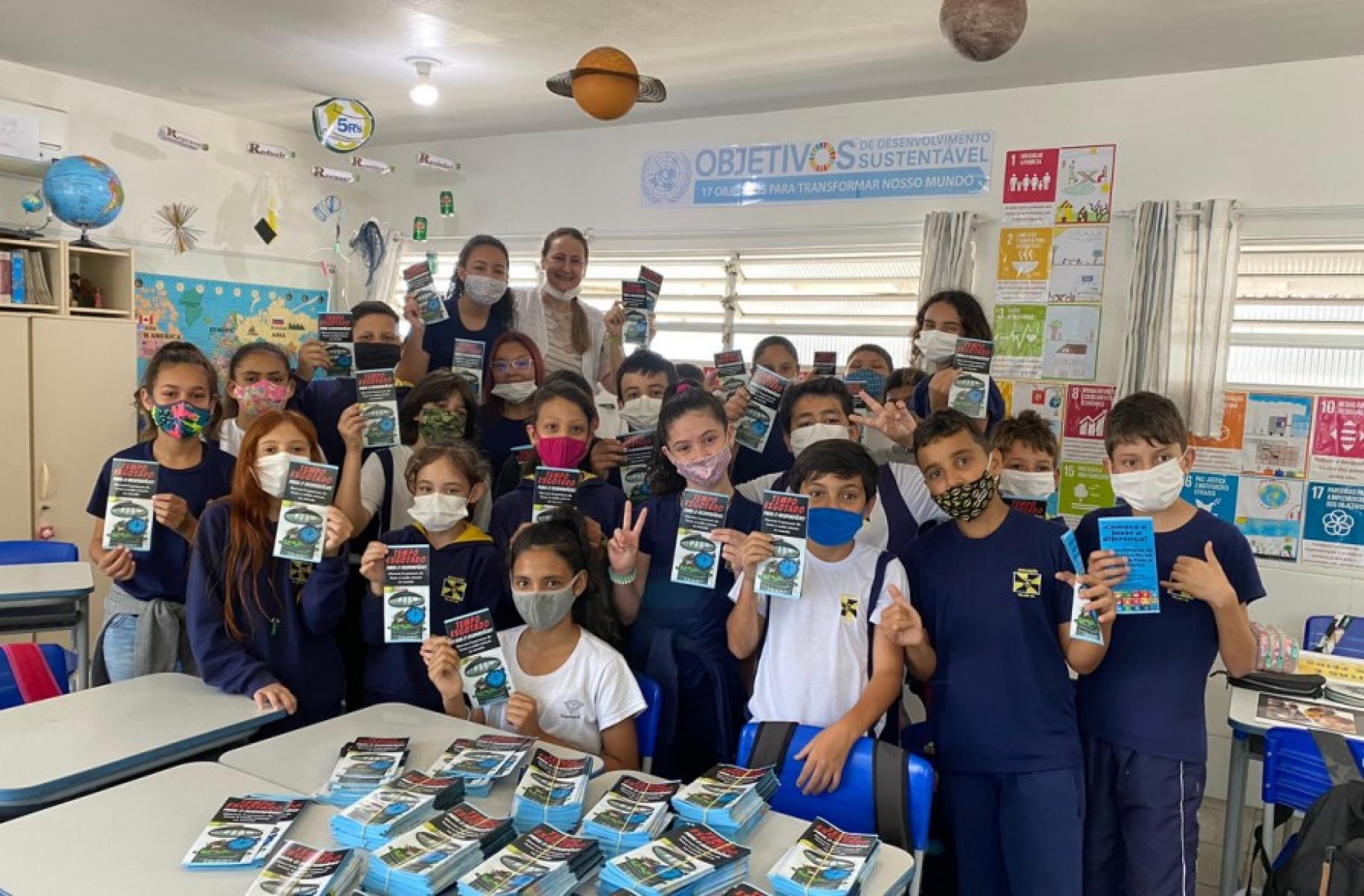 A group picture of classmates shows elementary school students and their teacher standing next to each other, wearing facemasks and displaying the results of their undertakings.