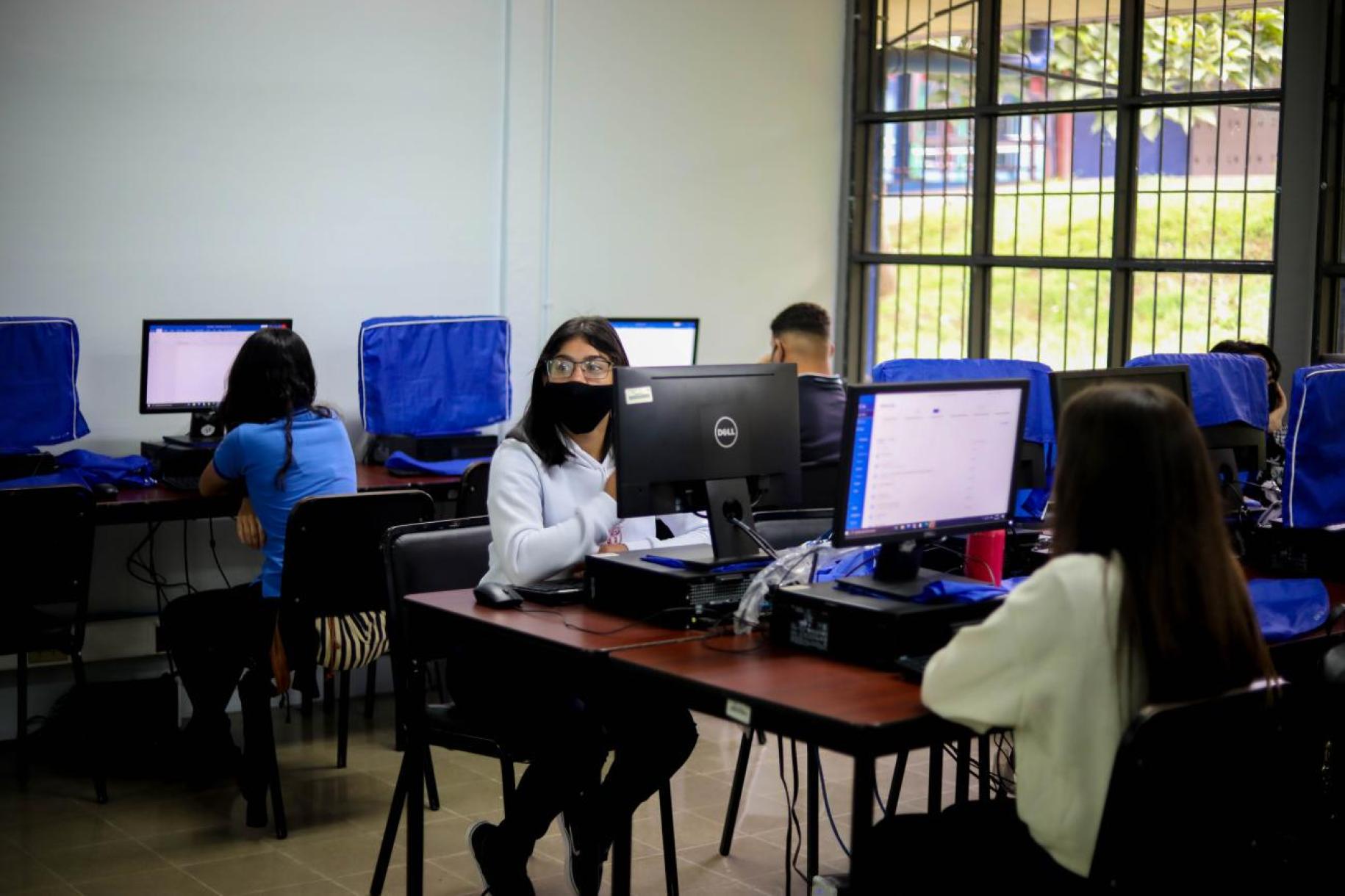 A group of students sitting in front of computer screens in a classroom.