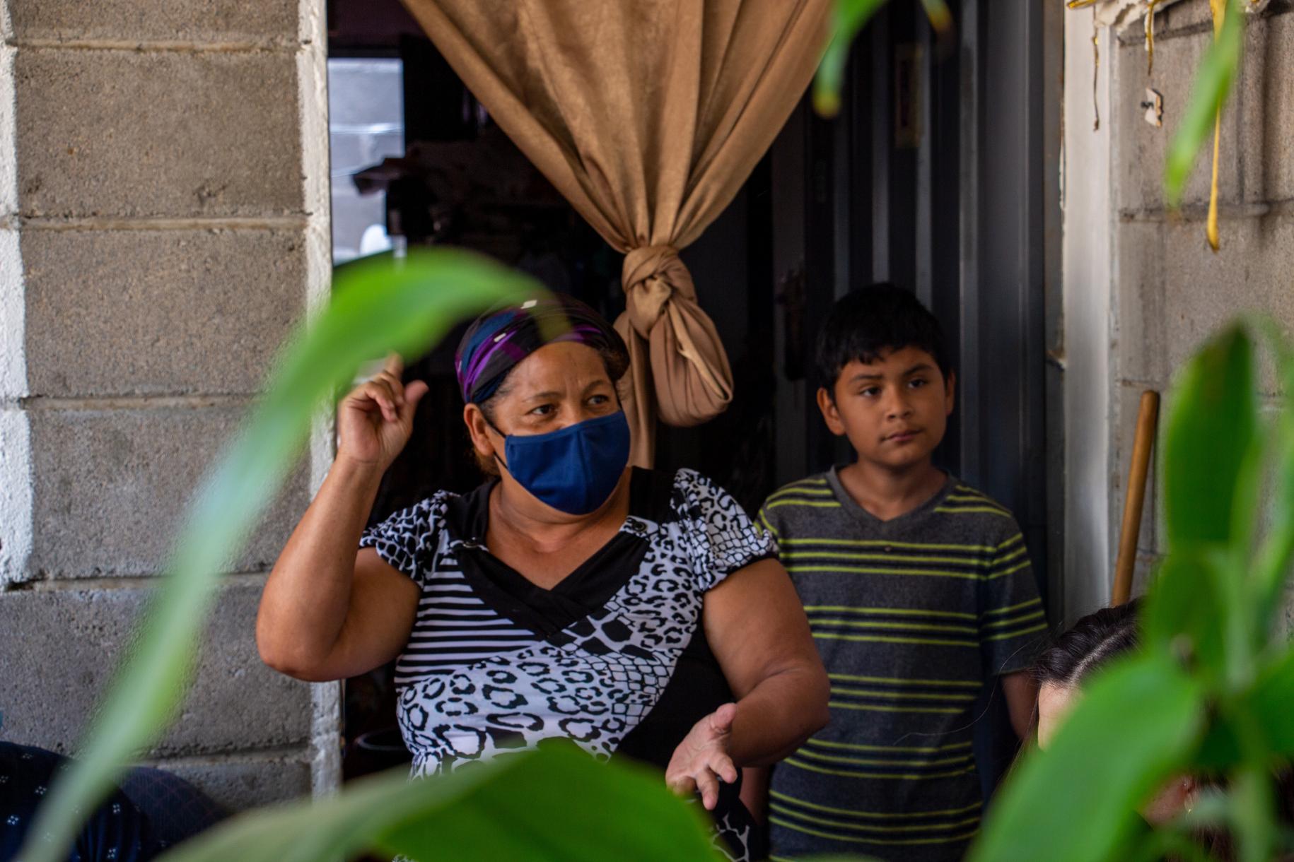 在一所房子的门外，一个戴着面具的女人和一个孩子与站在镜头外的人交谈。
