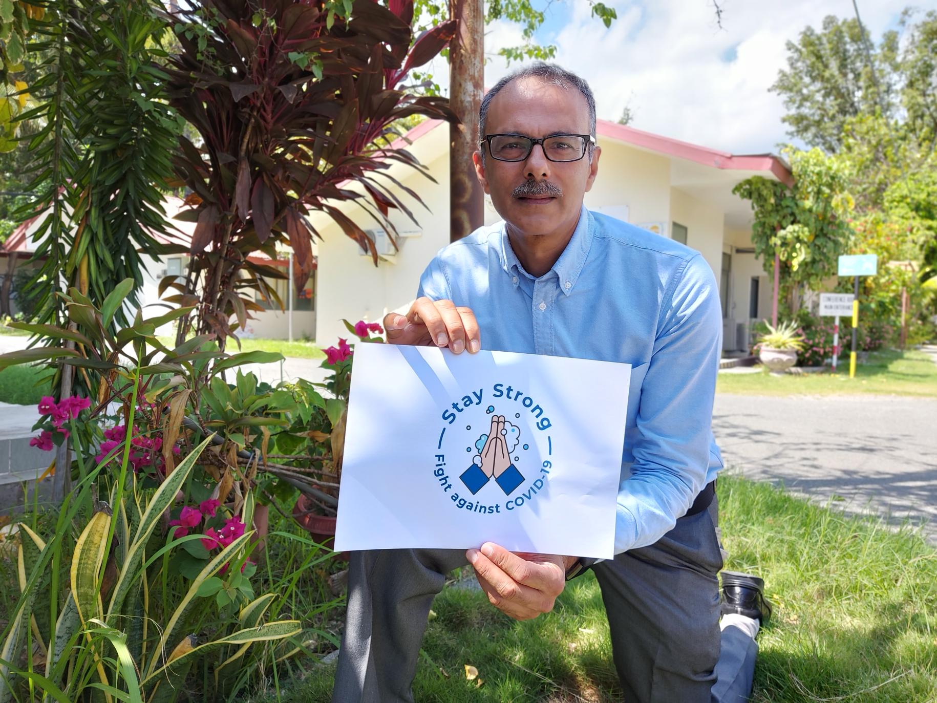 El Coordinador Residente saliente de Timor-Leste, Roy Trivedy, se arrodilla con un cartel para fomentar el lavado de manos durante la COIVD-19.