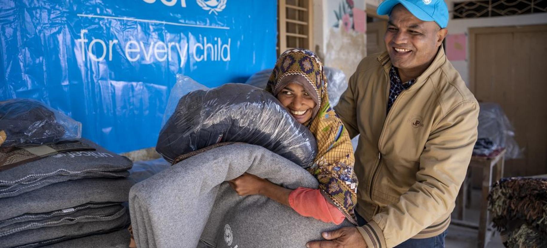 A man and a girl hold blankets and smile in front of a UNICEF sign.