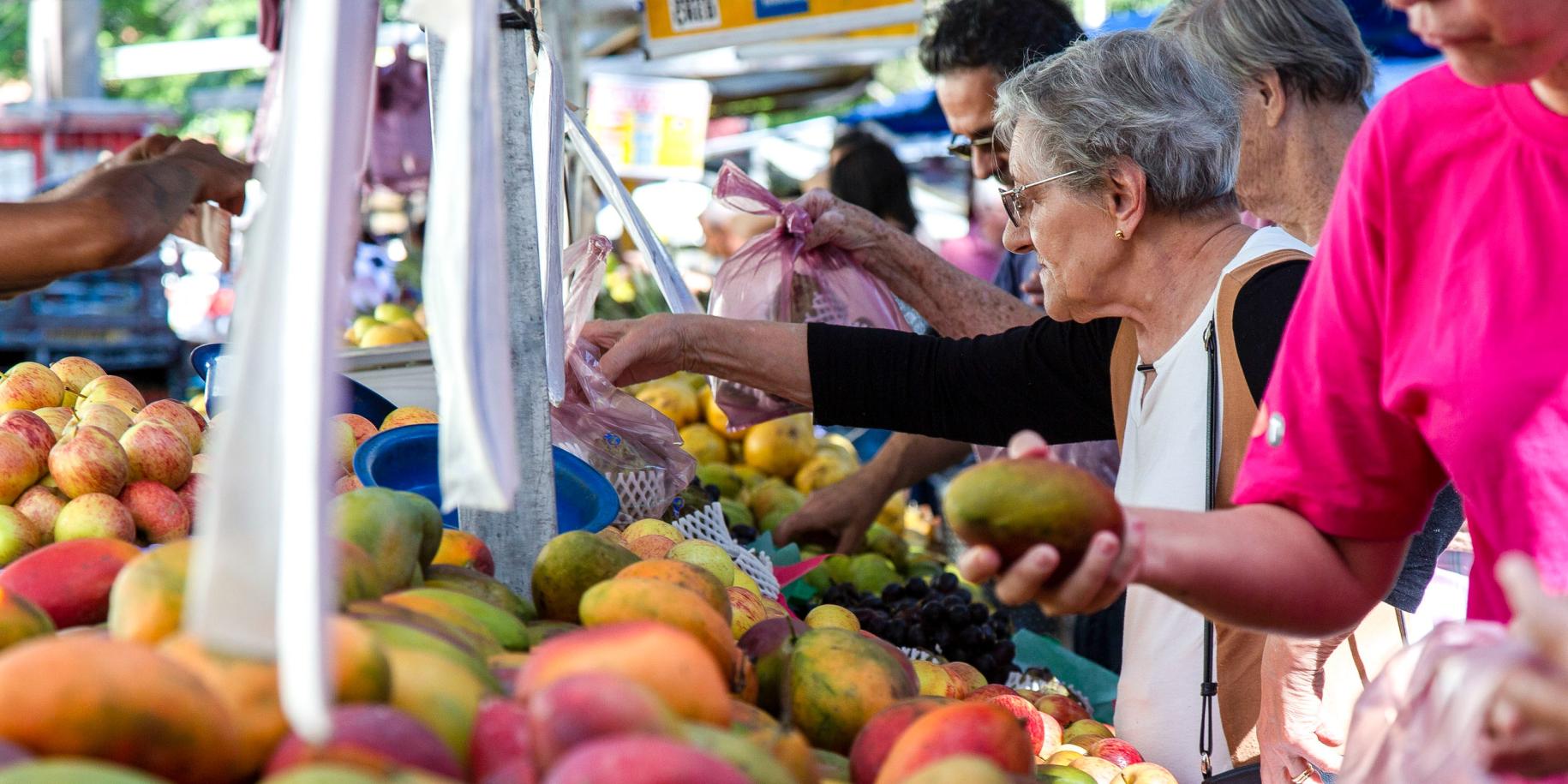 woman in market reaches for bag of pears