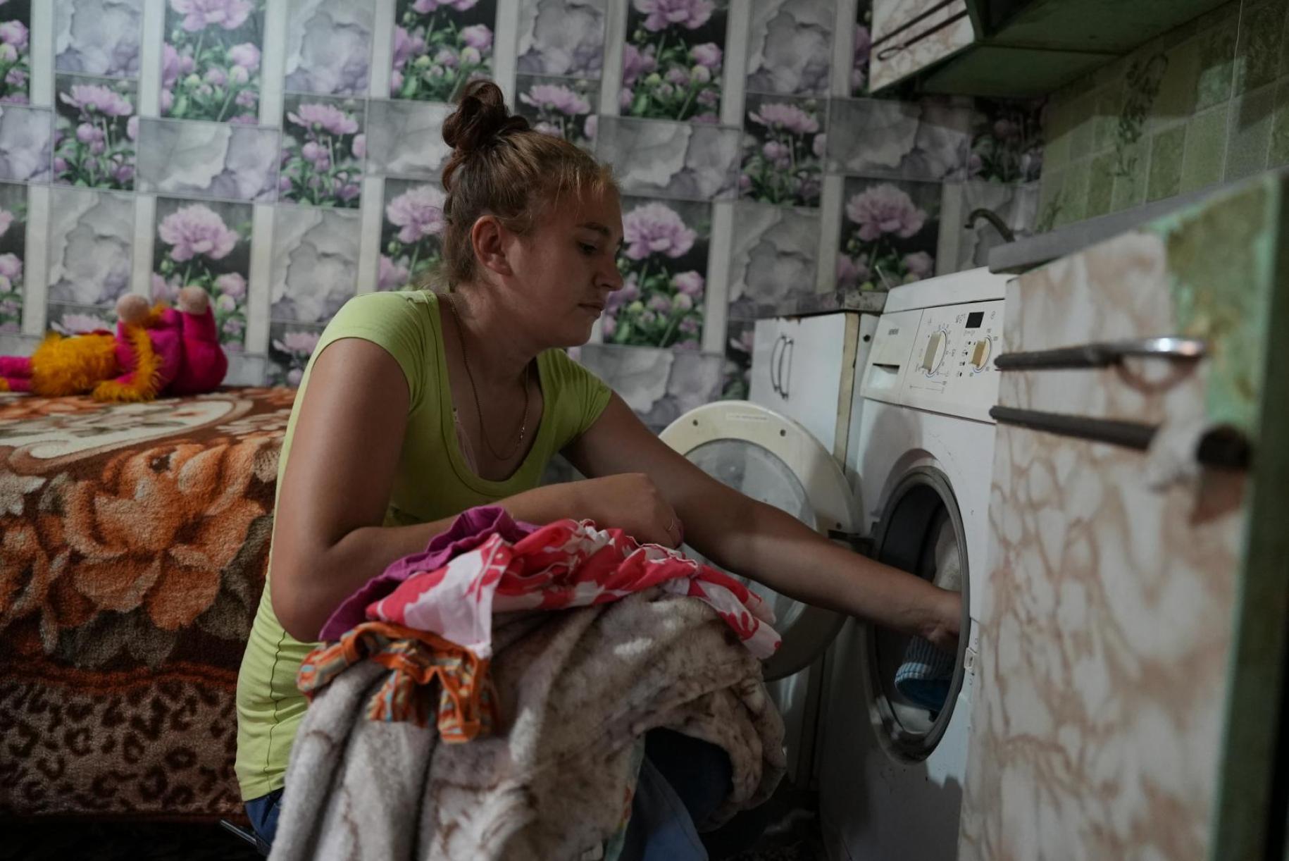 A woman puts clothes into a washing machine in a lightly-lit room.