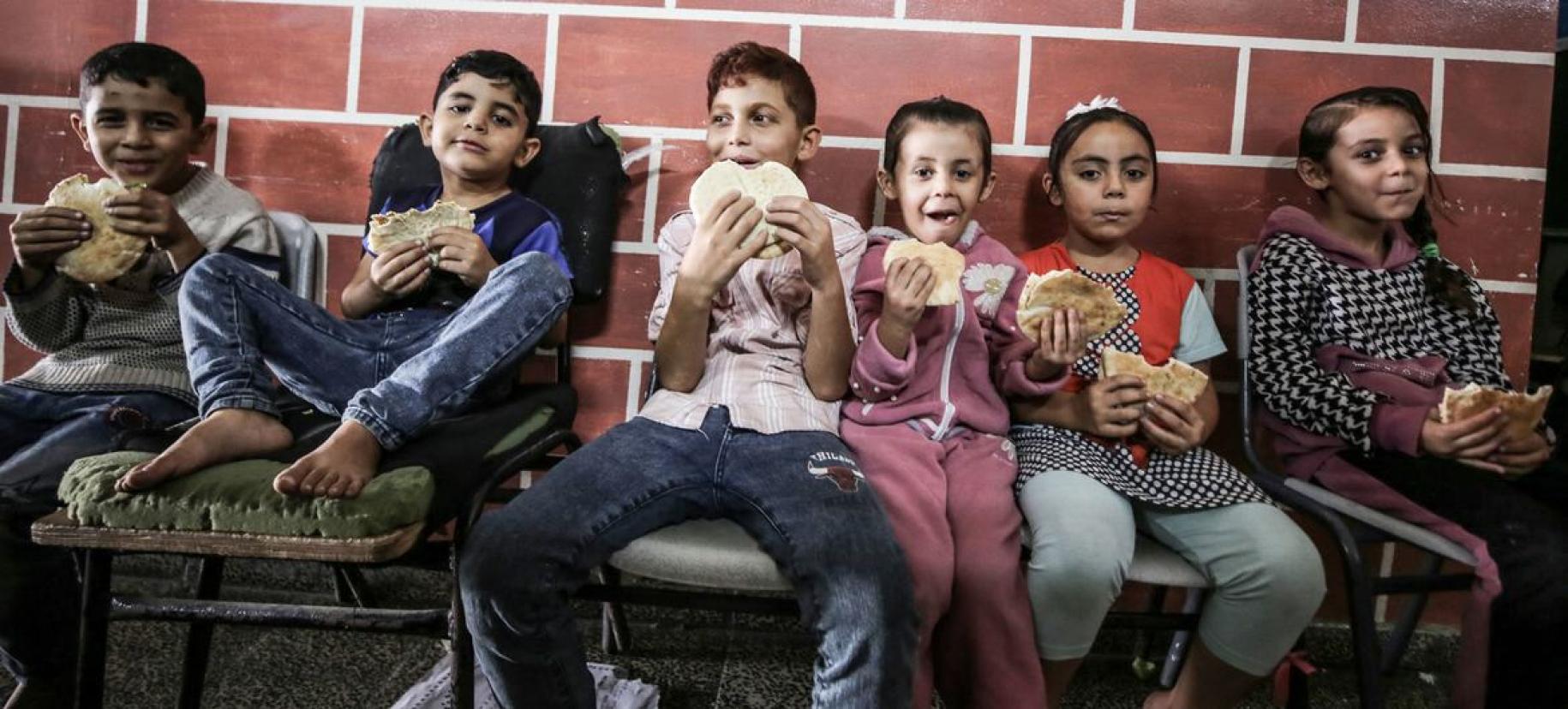 Children in Gaza eat bread in a school where communities are taking refuge