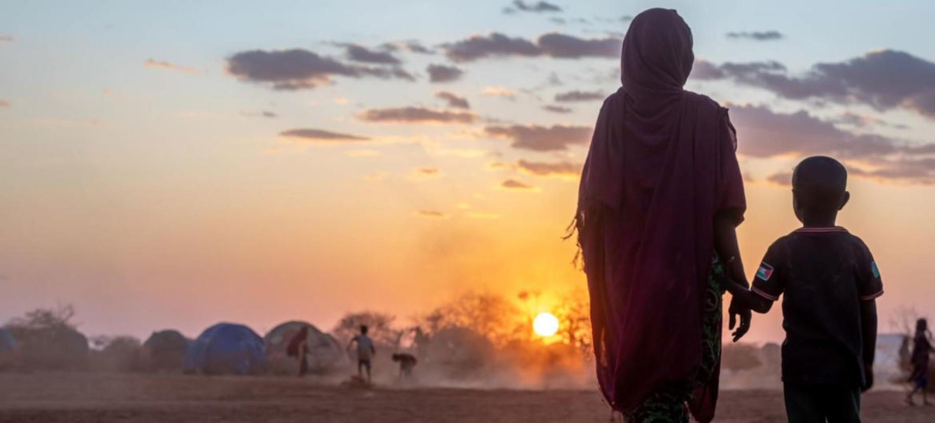 Фотография женщины и маленького мальчика, на фоне закатного солнца, в лагере для беженцев.