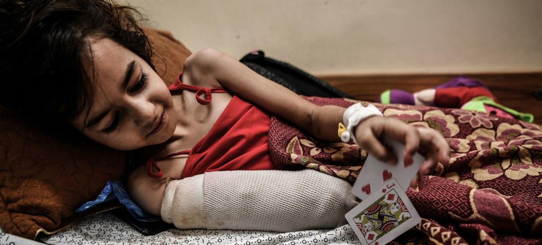 A young girl wearing a cast/covering on her arm plays with cards.