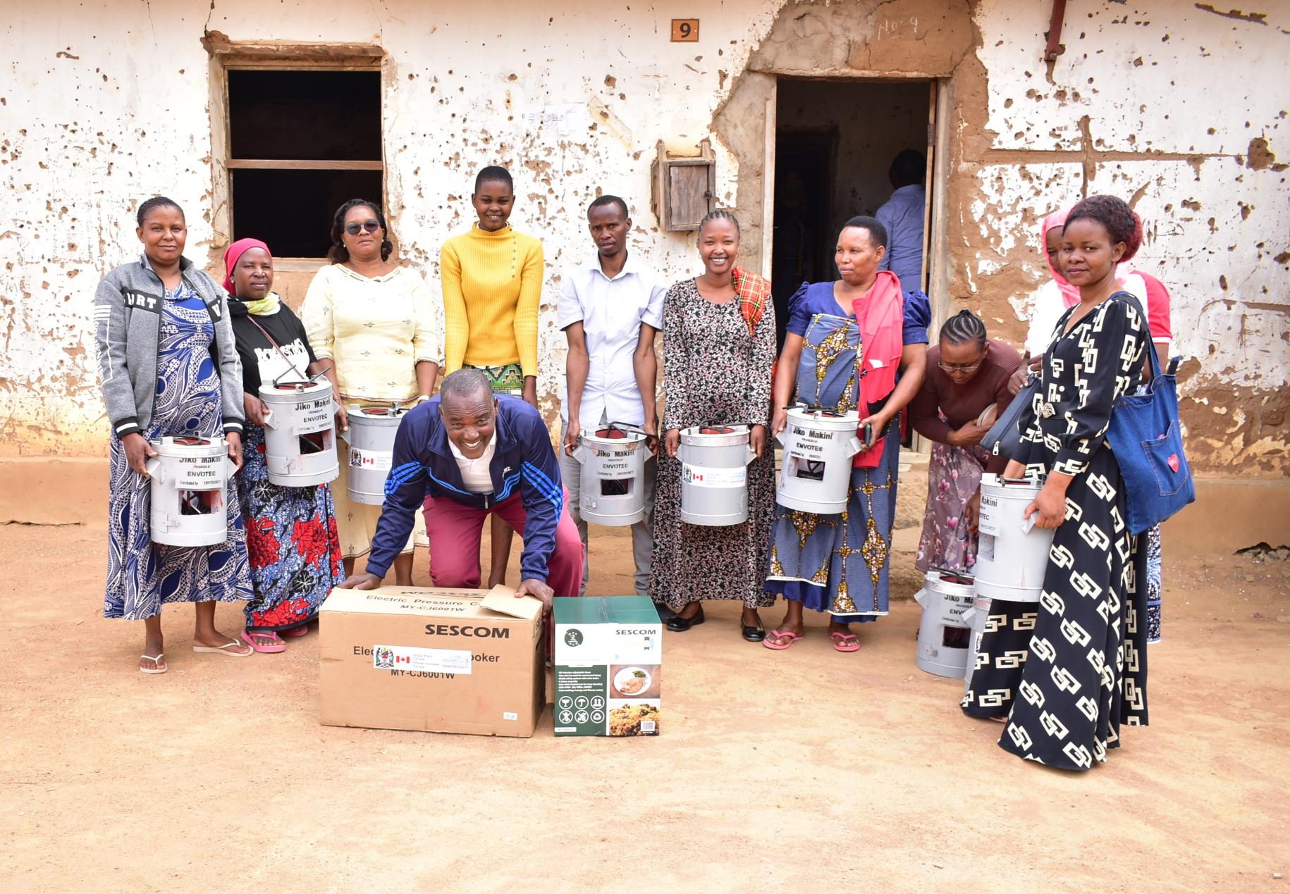 A group of women in a semi-circle and a man in the center hold small energy-saving stoves. 