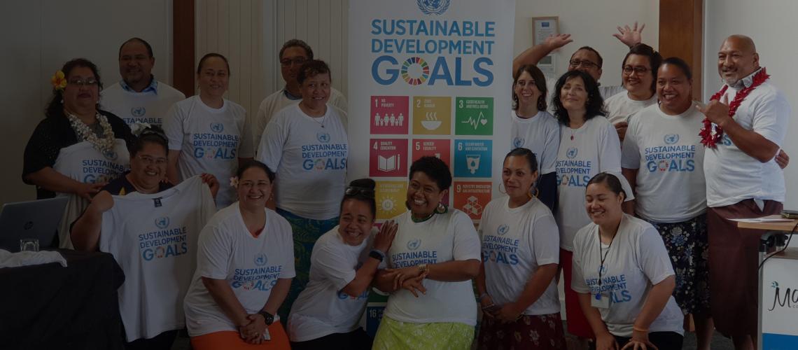 Un alegre grupo de representantes de la ONU, del gobierno, de las ONG y del sector privado que sonríen mientras llevan camisetas blancas con los Objetivos de Desarrollo Sostenible y están junto a una pancarta de los ODS.