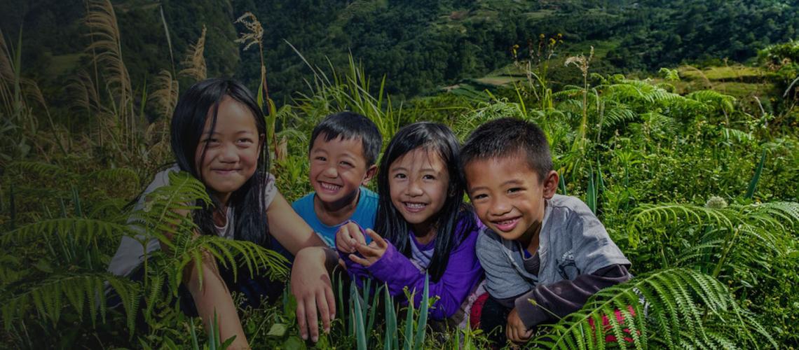 Children cheerfully sit in a field of grass and plants in Benguet Province, Philippines.