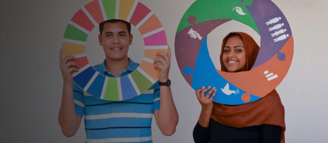 Two university students smile as they hold SDG-related wheels. 