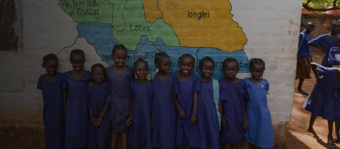 Little girls stand against a painted wall with a map of South Sudan. 