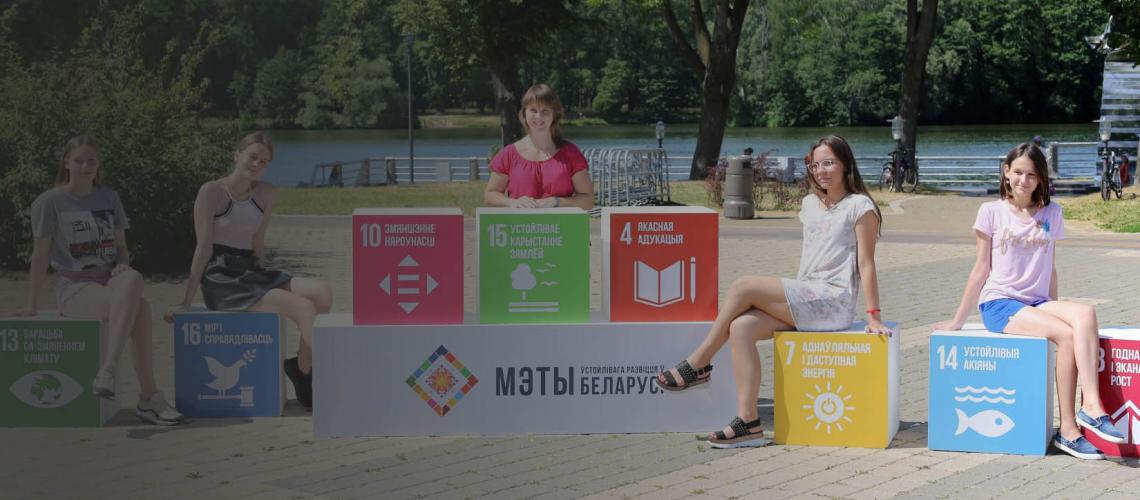 Una mujer y cuatro niñas están sentadas o de pie cerca de los bloques con los colores y símbolos de los ODS.