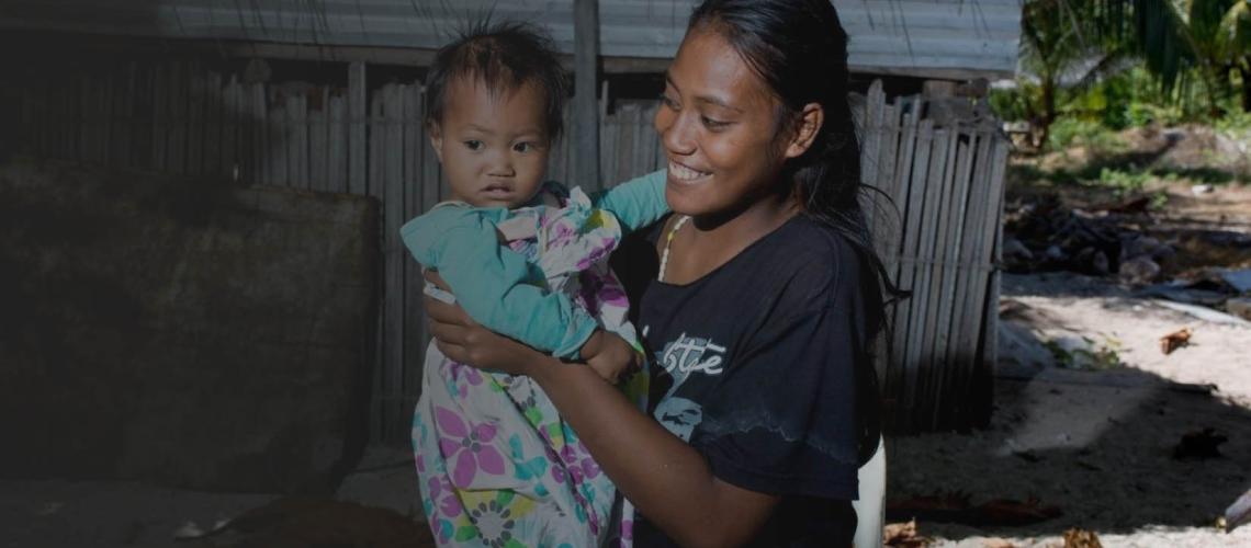 A young woman smiles as she holds a baby girl in her arms.