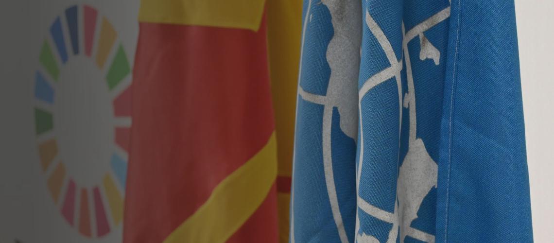 Primer plano de las banderas de Macedonia del Norte y de la ONU junto a el logo circular de los 17 ODS.