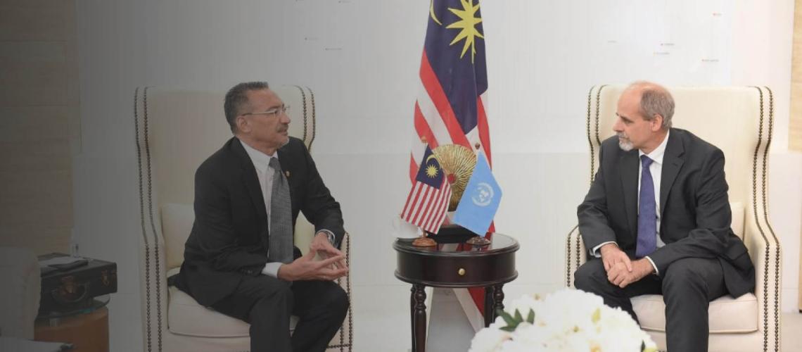 Stefan Priesner, UN Resident Coordinator for Malaysia, Singapore and Brunei Darussalam and YB Dato' Seri Hishammuddin Tun Hussein, Minister of Foreign Affairs Malaysia sit together on two chairs with a flag in between them.