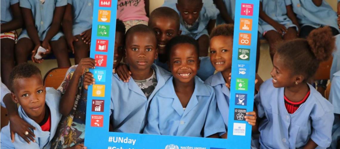 A group of smiling children holding a blue sign with the United Nations Sustainable Development Goals. 
