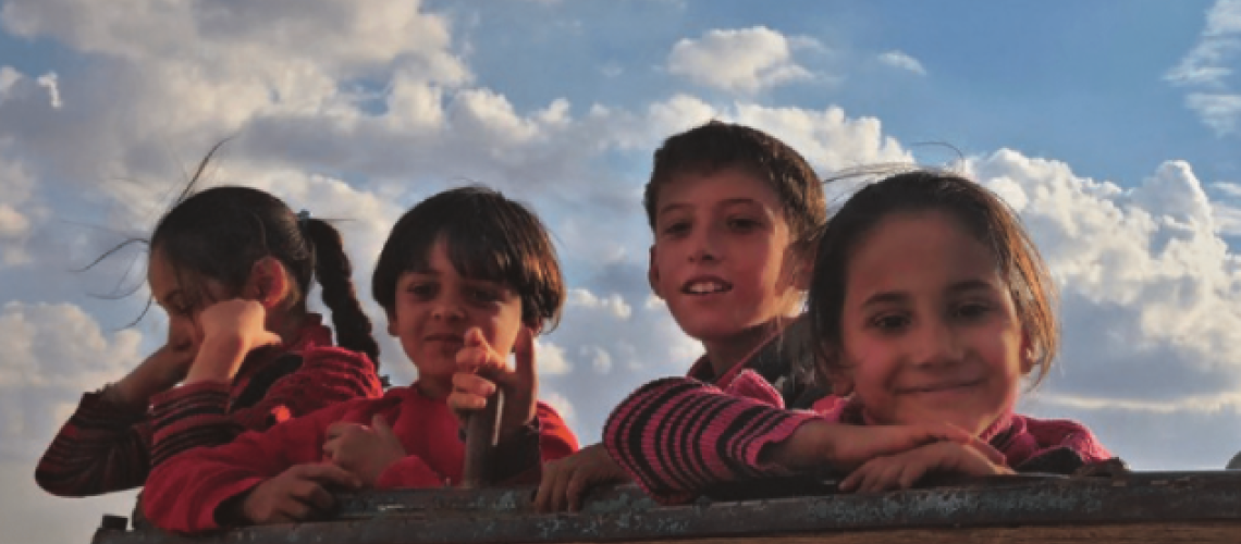 An image of four children smiling over a wall on a beautiful day. 