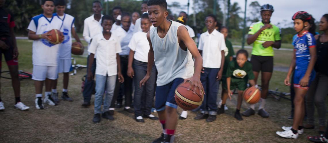 Un grupo de jóvenes observan a un joven que dribla una pelota de baloncesto.