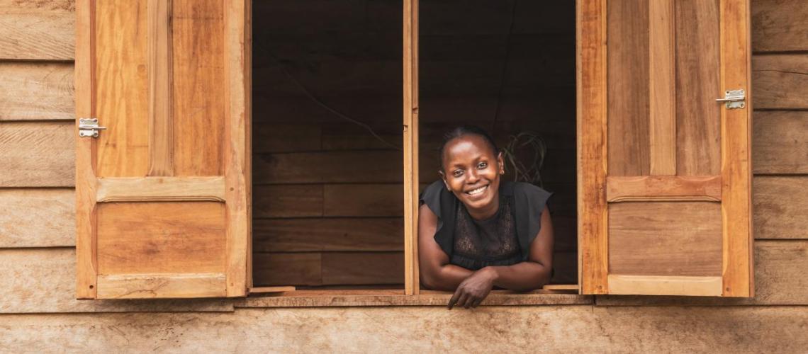 A smiling young woman leans out of a home through a window. 