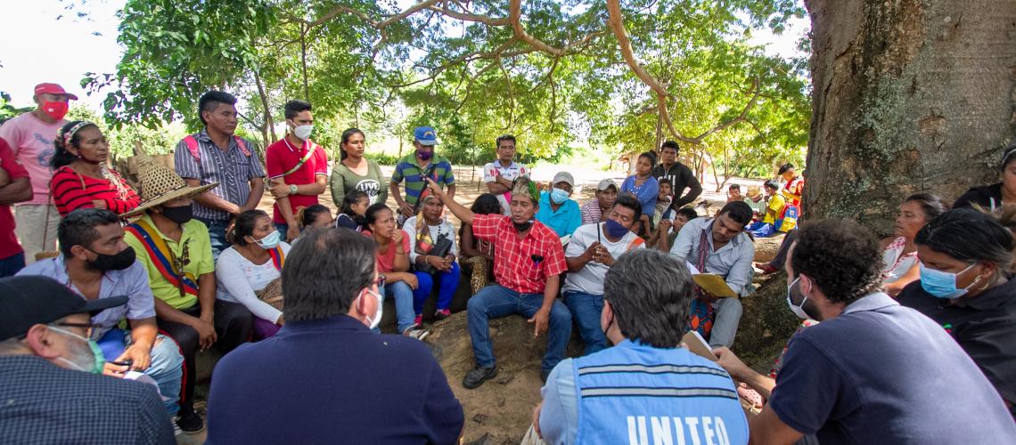 Un gran grupo de personas sentadas en el suelo bajo un árbol, durante un encuentro entre miembros de una comunidad de la etnia Yukpa y representantes del equipo de la ONU en Venezuela, en el estado Zulia.