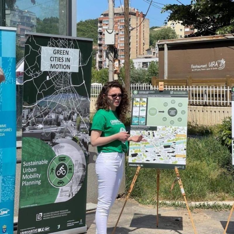 A woman stands next to two large posters describing climate action in Kosovo*.