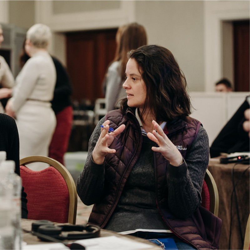 A woman expresses something, using her hands, while in a seminar setting.